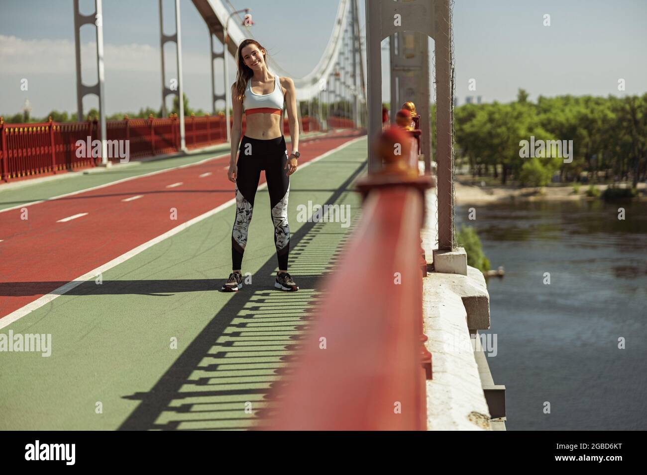 Glückliche athletische Frau in moderner Sportkleidung posiert für Kamera auf Fußgängerbrücke Stockfoto