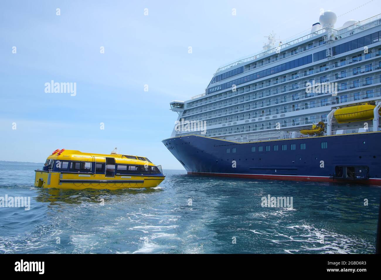 Schiff vor Anker im St. Peter Port, Guernsey. Großes Schiff mit blauem Rumpf und einem gelben Rettungsboot oder Tender vor der Küste, Kanalinseln, großbritannien. Stockfoto