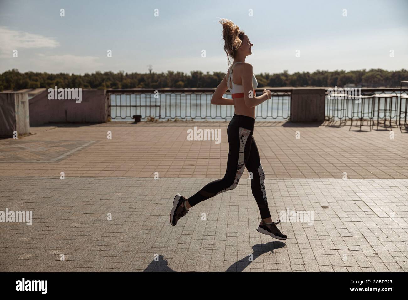 Lady in Sportswear und Sneakers mit lockeren Haaren läuft entlang leerer Stadtwälle Stockfoto
