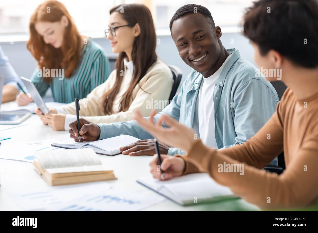 Eine vielfältige Gruppe von Studenten, die am Schreibtisch sitzen, schreiben und sprechen Stockfoto