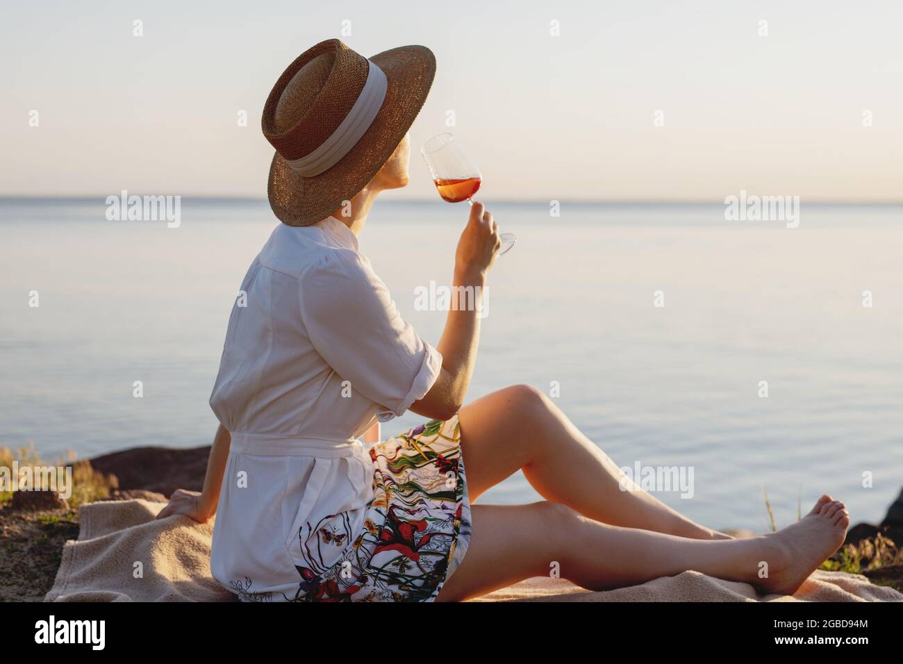 Schöne Dame im Strohhut mit einem Glas Wein am Strand. Stockfoto