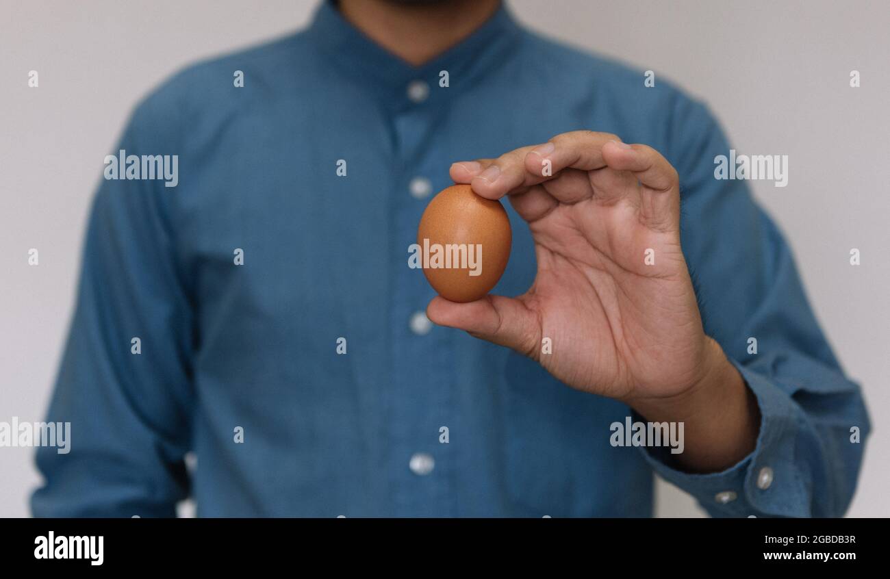 Männliche Hand hält Ostern braun Huhn Ei isoliert auf grauem Hintergrund Stockfoto