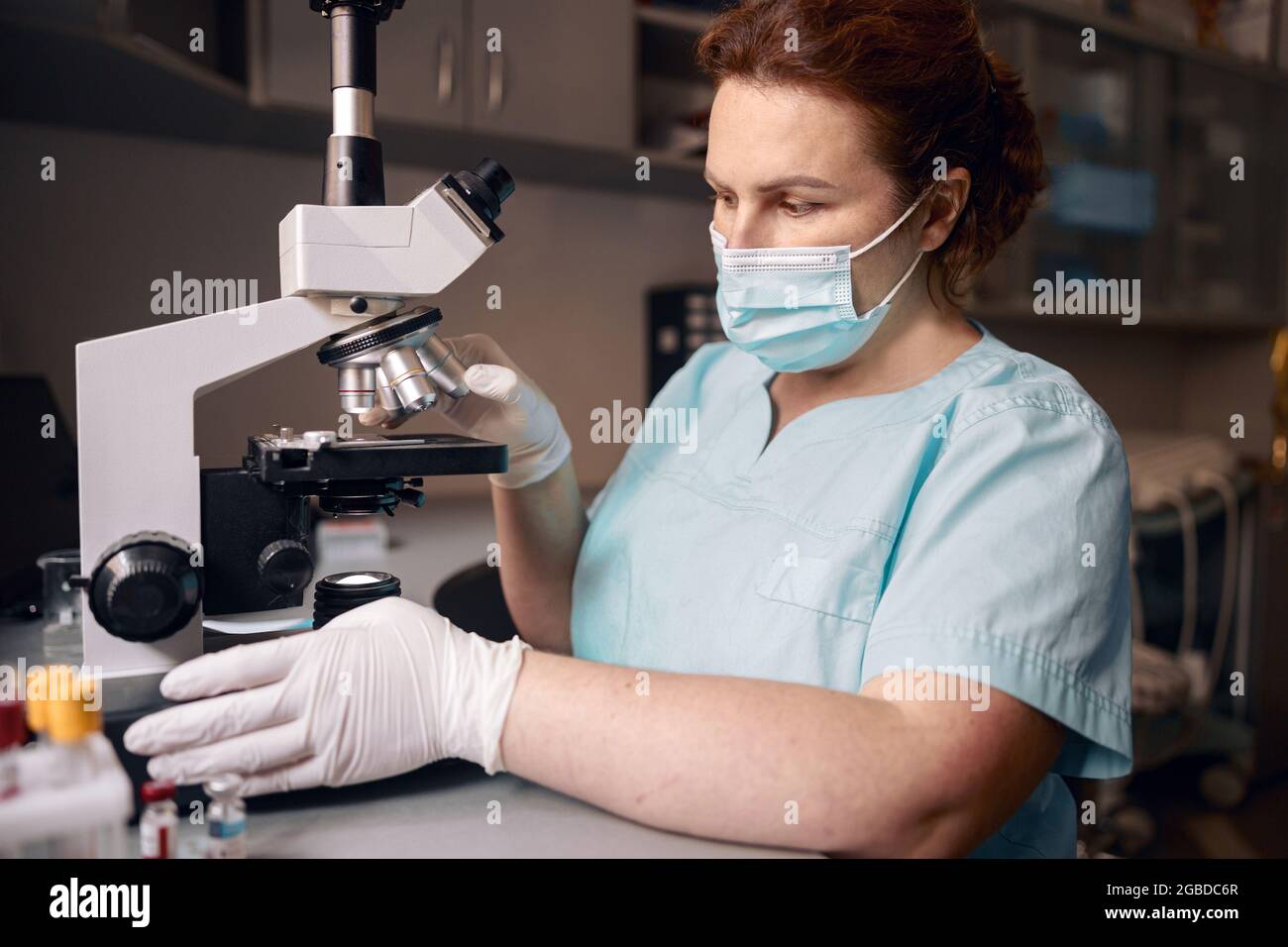 Frau Laborassistentin arbeitet mit dem Mikroskop, um Materialproben in der Klinik zu erforschen Stockfoto