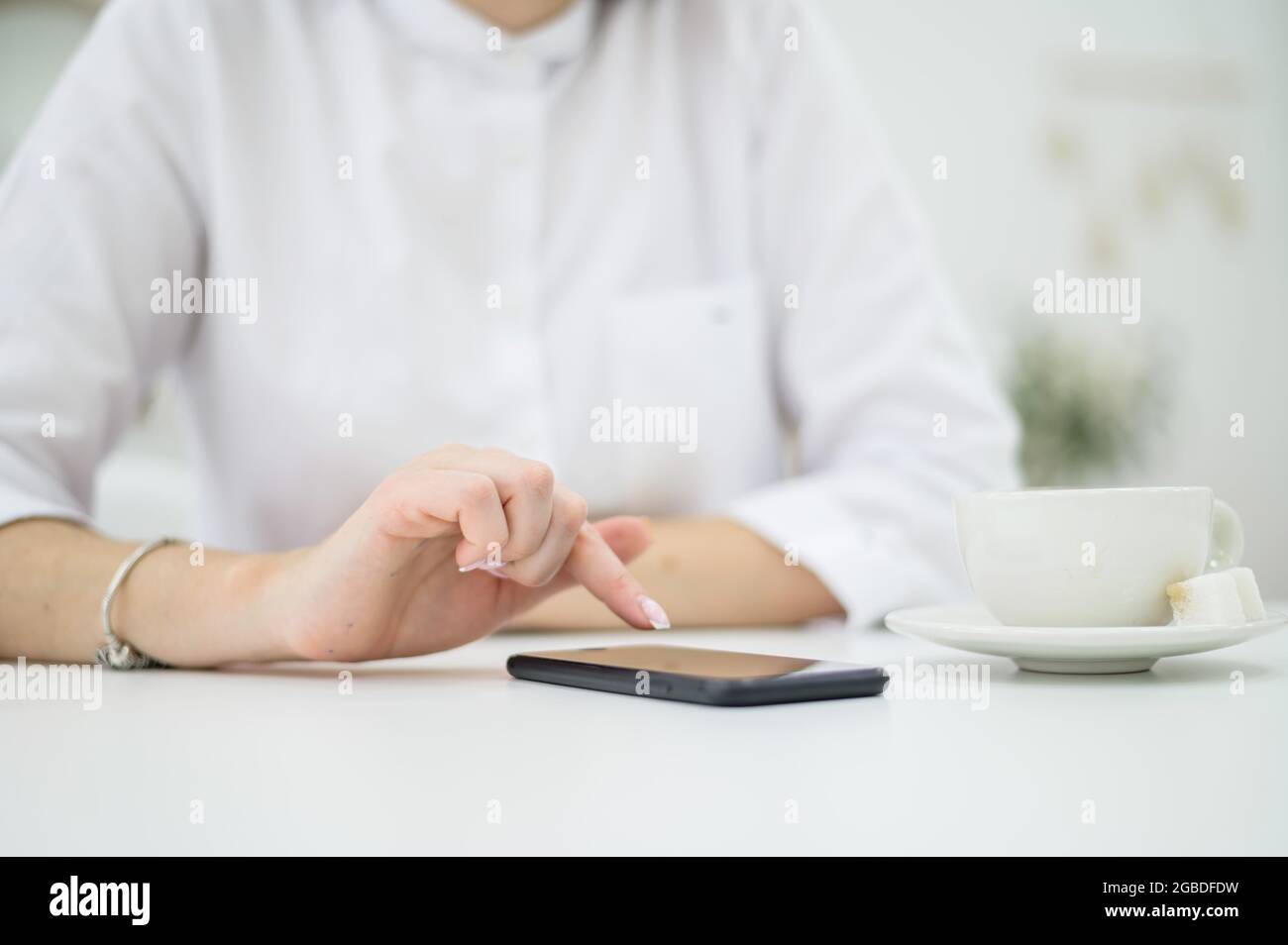 Eine Frau in einem weißen Hemd mit gepflegten Händen und frischer Maniküre trinkt Kaffee in einem Café. Mädchen schreibt mittags eine Nachricht auf ein Smartphone Stockfoto