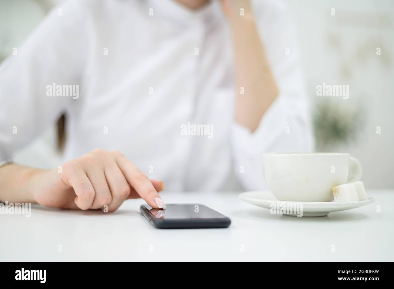 Eine Frau in einem weißen Hemd mit gepflegten Händen und frischer Maniküre trinkt Kaffee in einem Café. Mädchen schreibt mittags eine Nachricht auf ein Smartphone Stockfoto