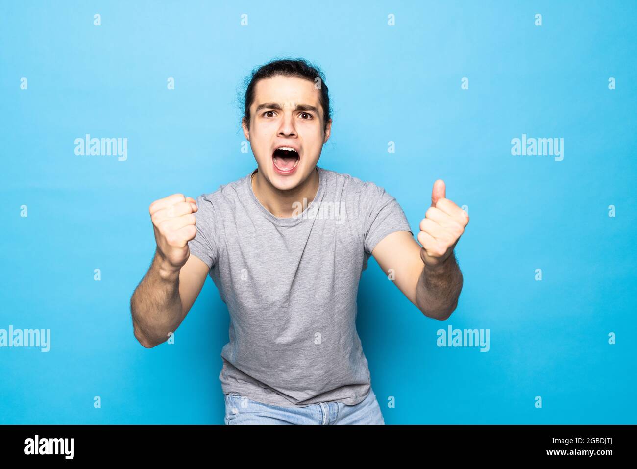 Begeisterter Sieger, der mit den Fäusten auf blauem Hintergrund steht. Stockfoto