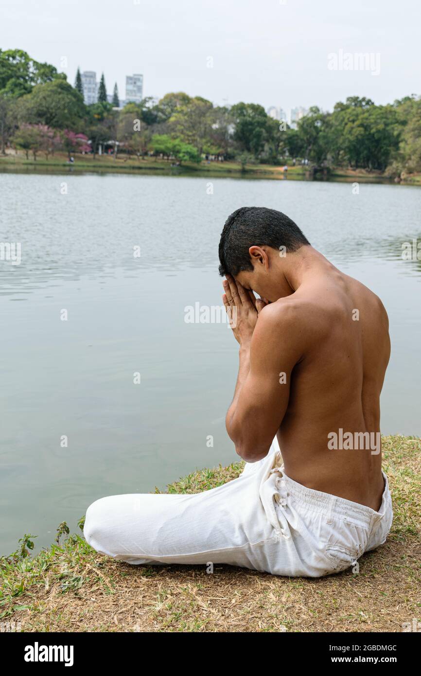 Brasilianischer junger Mann sitzt an einem See in einer dankbaren Position. Stockfoto