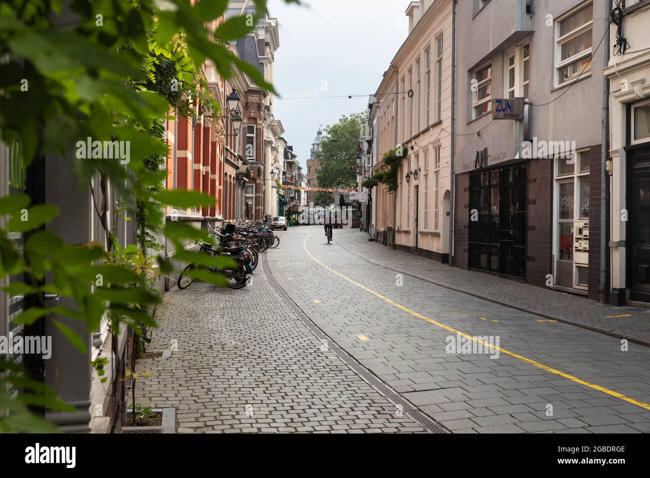 Breda, Niederlande 28. Juni 2021. Straße im Stadtzentrum mit alten historischen Gebäuden, einem Bürgersteig, Geschäften, Häusern, einem Radfahrer, Geparkte Fahrräder Stockfoto