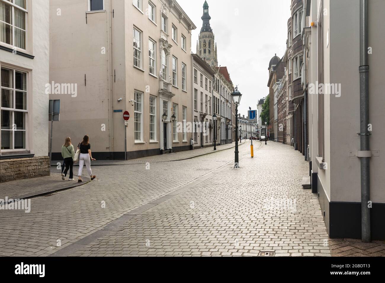 Breda, Niederlande 28. Juni 2021. Straße im Stadtzentrum mit alten historischen Gebäuden mit hellen Fassaden, einem Bürgersteig, einer Kirche und Menschen Wal Stockfoto