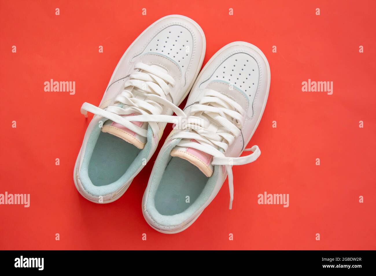 Weiße Sneakers isoliert auf rotem Hintergrund mit Kopierraum. Draufsicht. Flach liegend. Sportbekleidung. Damenschuhe. Stockfoto