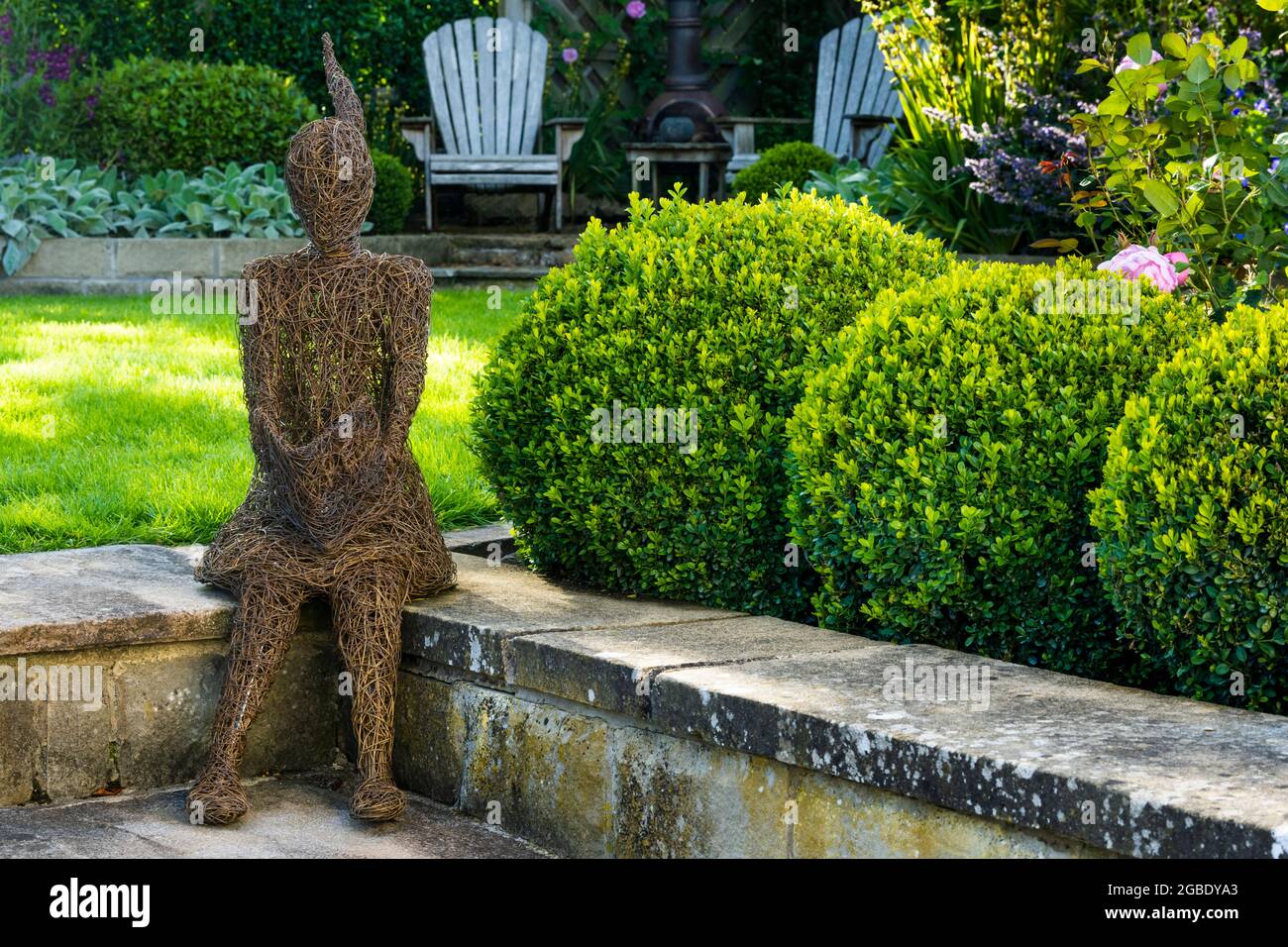 Skulpturenkunst (ornamentales Merkmal) in einem wunderschönen Landschaftsgarten (mehrjährige Pflanzen, Sträucher, geclippte Kastenbälle, Rasen, Stühle) - Yorkshire England UK Stockfoto