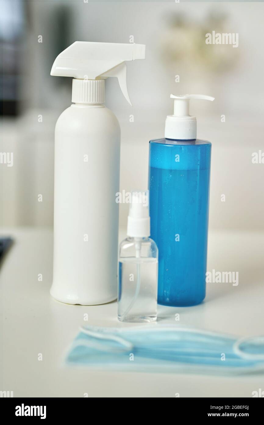 Nahaufnahme von Reinigungsmitteln, Desinfektionsmittel-Spray und Gel in Flaschen, Gesichtsschutzmaske auf Küchenoberfläche Stockfoto