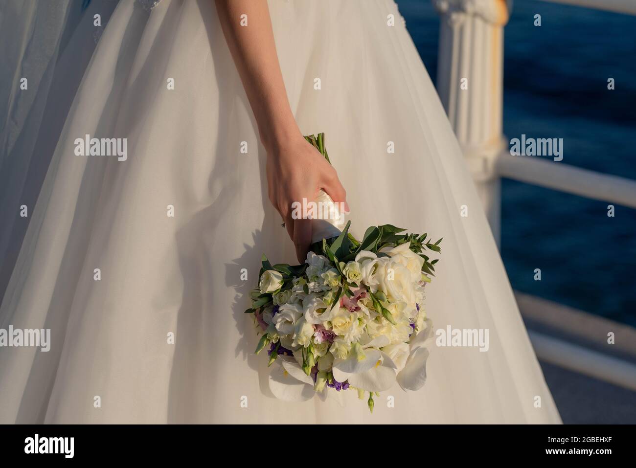 Die junge Braut trägt ein wunderschönes Hochzeitskleid aus Tüll und hält einen zarten Blumenstrauß in der Hand lässig am Körper, ein traditionelles florales Accessoire Stockfoto