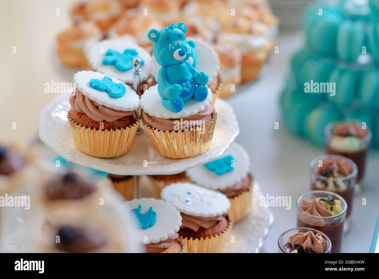 Entzückende Cupcakes mit blauen königlichen Eisbären-Figuren und Schokoladencreme, süße Leckereien auf gestapelten weißen Tellern, die für eine Dessertbar zubereitet werden Stockfoto