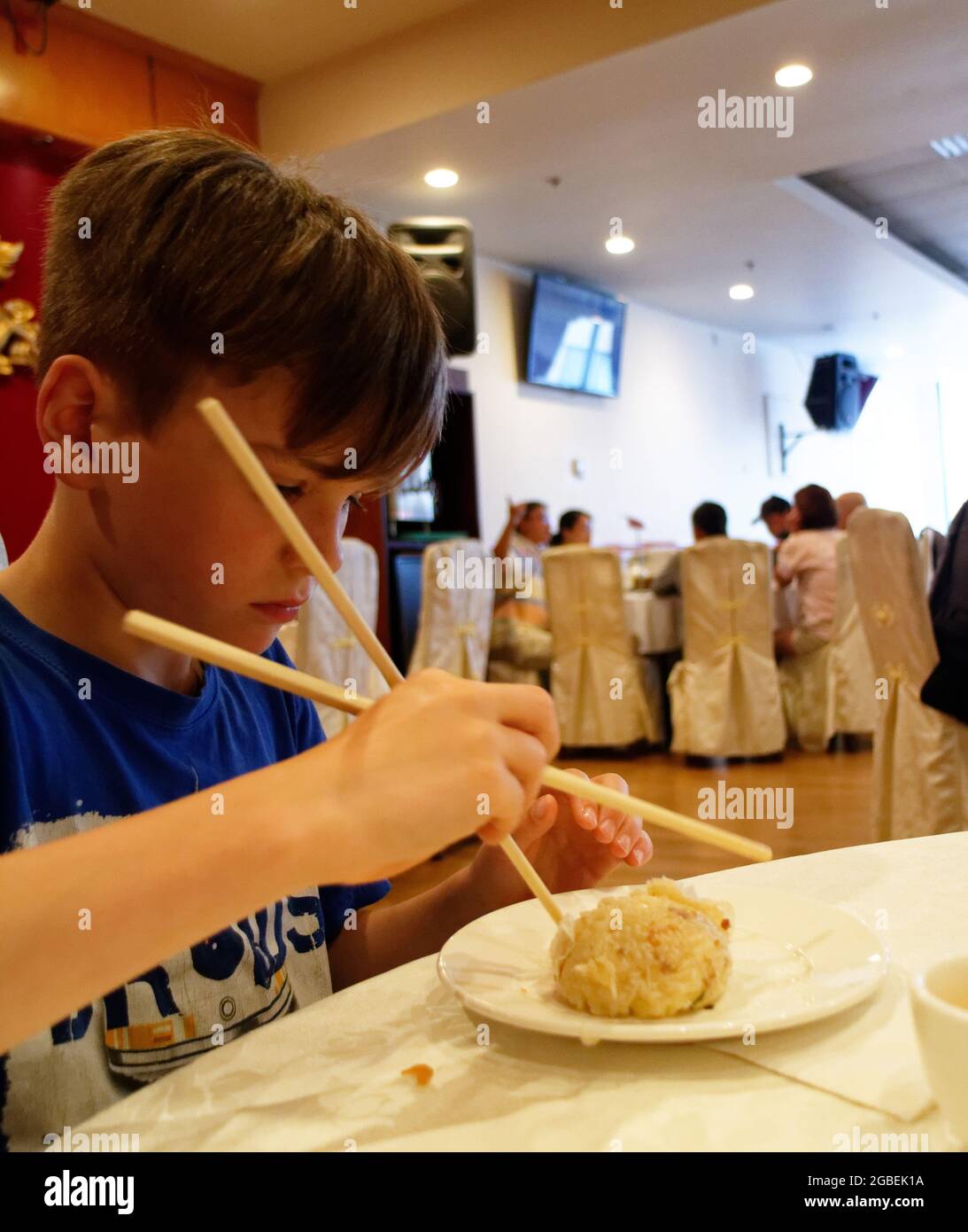 Ein kleiner Junge (9 Jahre), der mit Essstäbchen isst Stockfoto