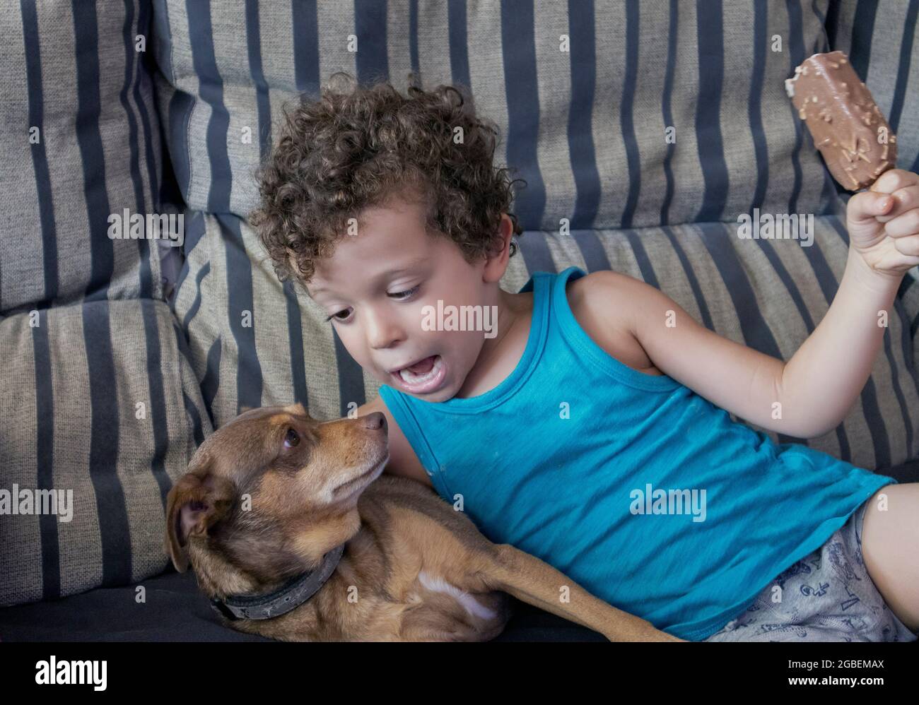 Der Welpe liegt auf dem Sofa, ein Kind hält ein Schokoladeneis in der Hand Stockfoto