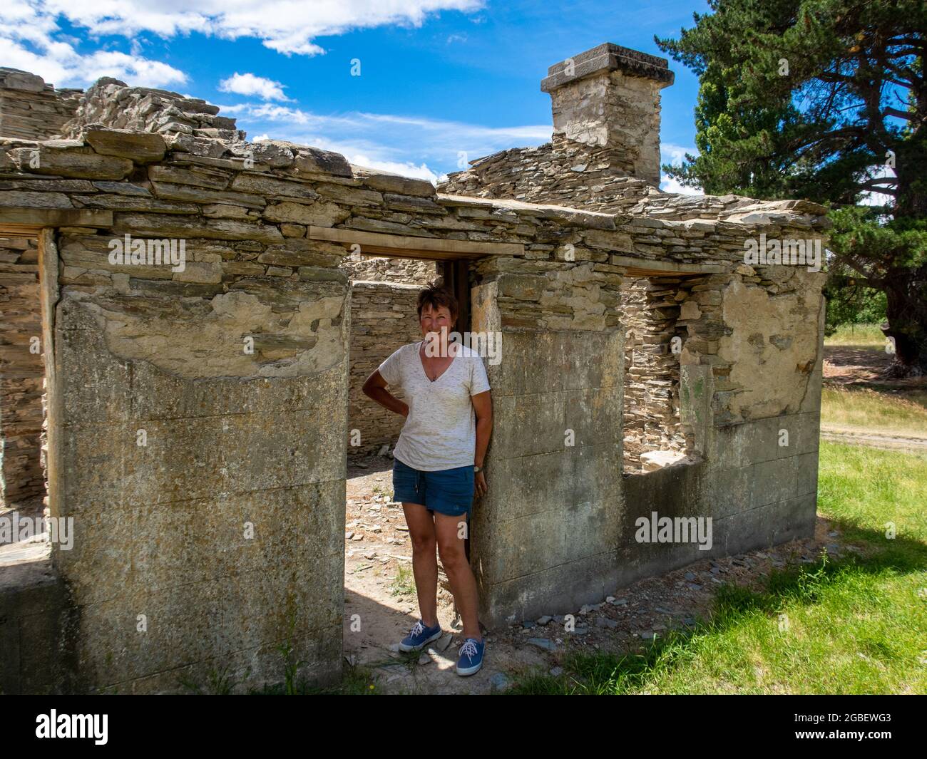 Auf einem öffentlichen Campingplatz in der Nähe des Lindis Passes in Zentral-Otago, Neuseeland, erkundet eine Touristenfrau die Überreste eines alten Hotels und einer alten Hütte Stockfoto