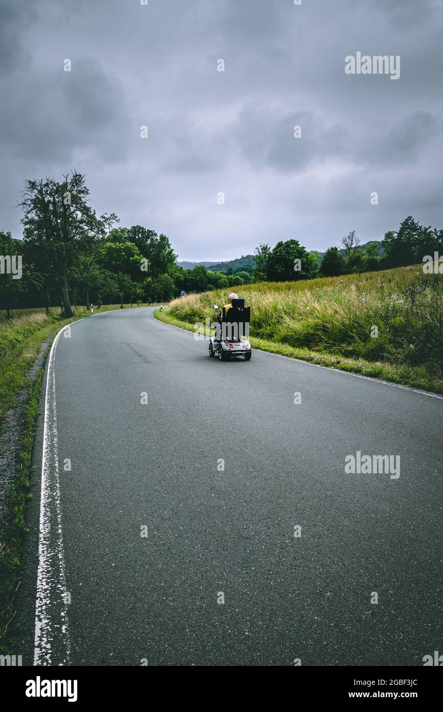 Vertikale Aufnahme einer leeren Straße auf dem Land an einem grau bewölkten Tag mit einem älteren Fahrer Stockfoto