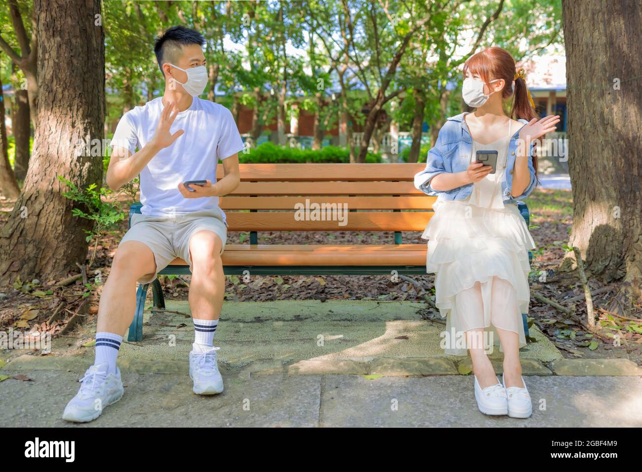 Junges Paar in sozialer Distanz und sitzt auf der Bank im Park Stockfoto