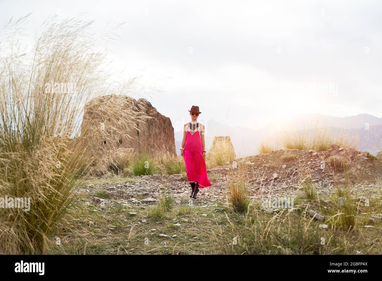 asiatische Frau in rotem Kleid, die in der Morgensonne an einem verlassenen historischen Ort spazieren geht Stockfoto