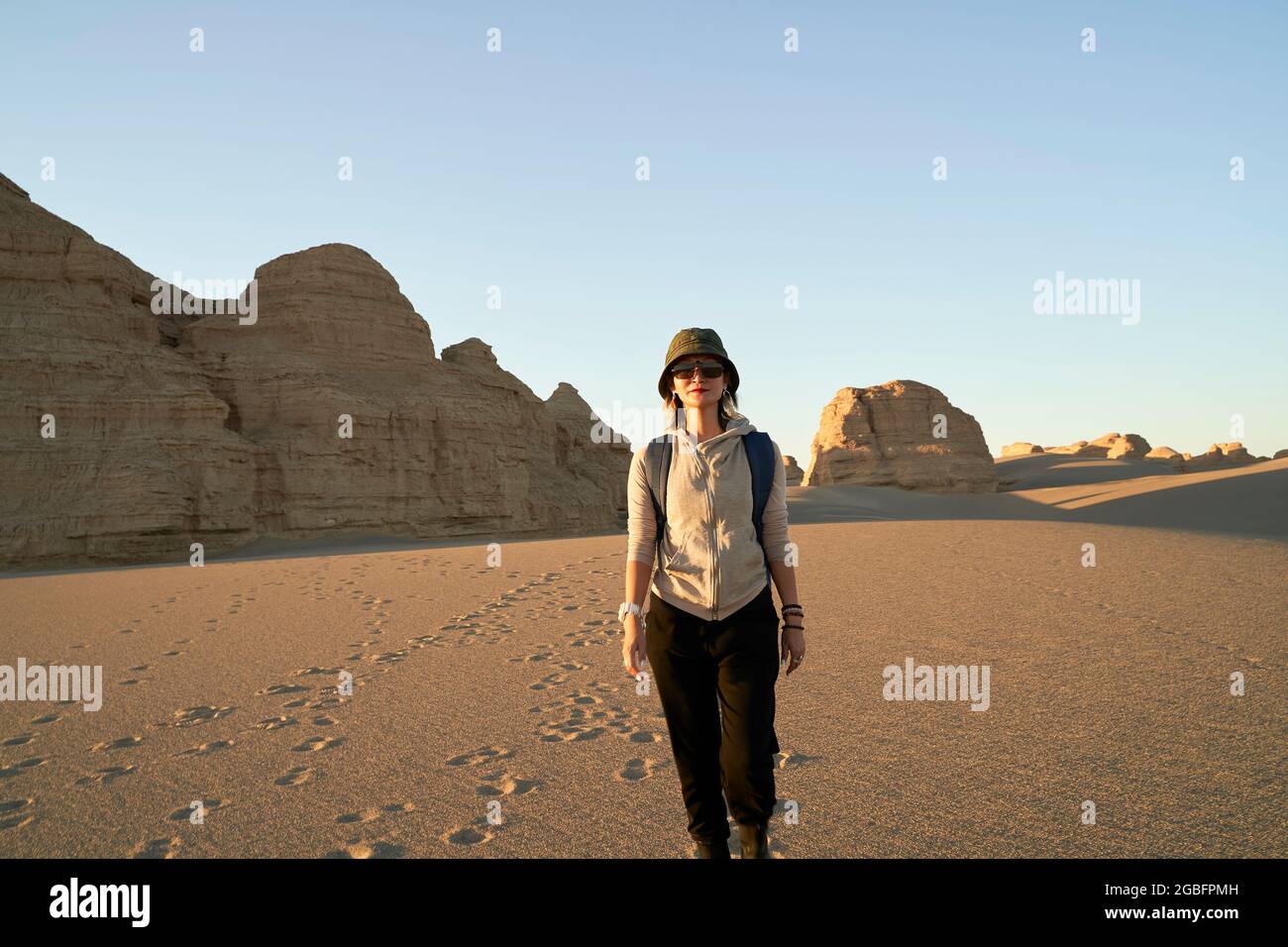 asiatische Frau Reisende Backpacker zu Fuß in der Wüste bei Sonnenuntergang mit Yardang Landform im Hintergrund Stockfoto
