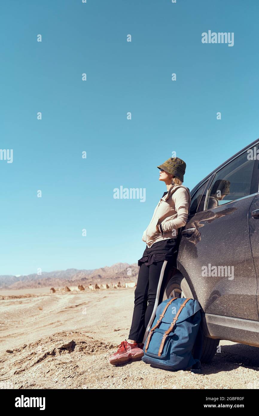 asiatische Frau, die sich gegen das Auto lehnt und die Aussicht in der wüste gobi betrachtet Stockfoto