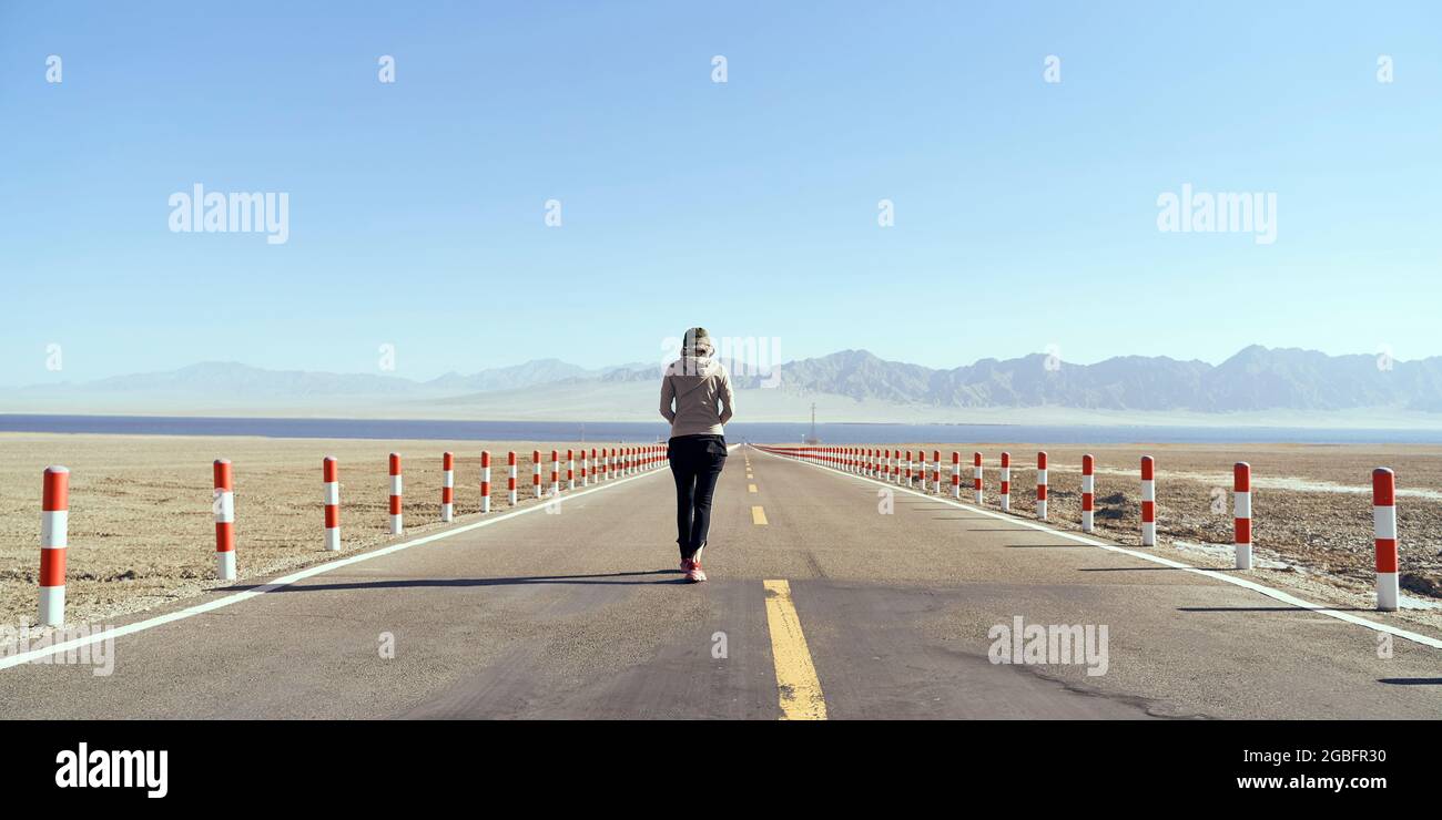 Rückansicht einer asiatischen Touristenfrau, die auf einer leeren Autobahn in Richtung eines Sees läuft Stockfoto