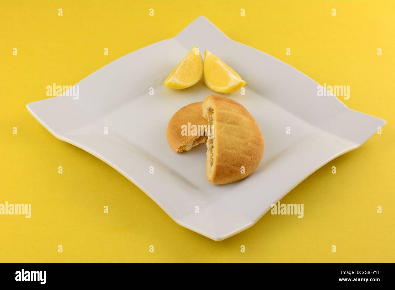 Griechische Zitronen-Shortbread-Pie-Hälften mit Zitronenscheiben auf weißem Snackteller auf gelbem Hintergrund Stockfoto