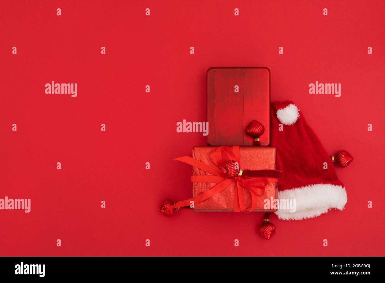 Draufsicht der Komposition des traditionellen Weihnachtsmannes Hut in der Nähe eingewickelte Geschenke am Weihnachtstag vor rotem Hintergrund platziert Stockfoto