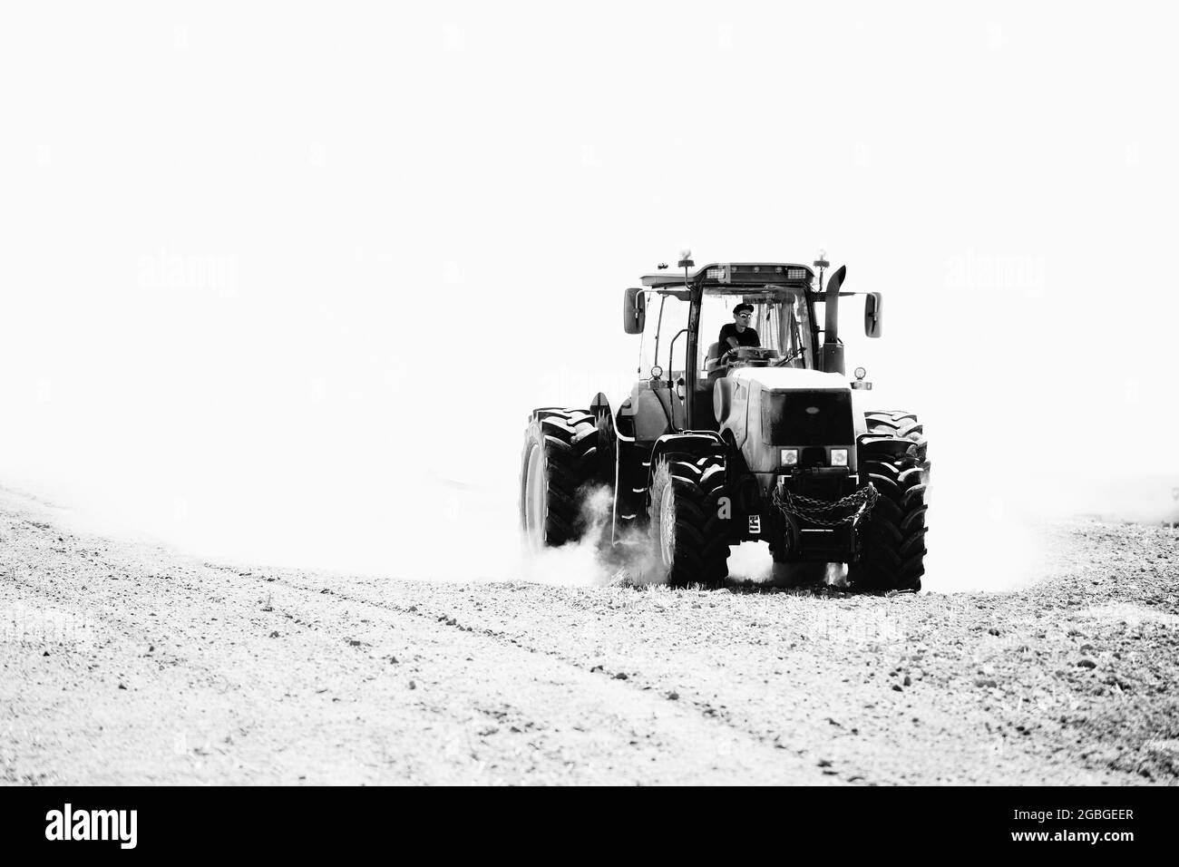 Grodno - April 2021: Landwirtschaftliche Industrie Traktor Anbau auf dem Feld in Wolken von Staub hoher Kontrast schwarz-weiß-Bild. Selektive Fokusfarm Stockfoto