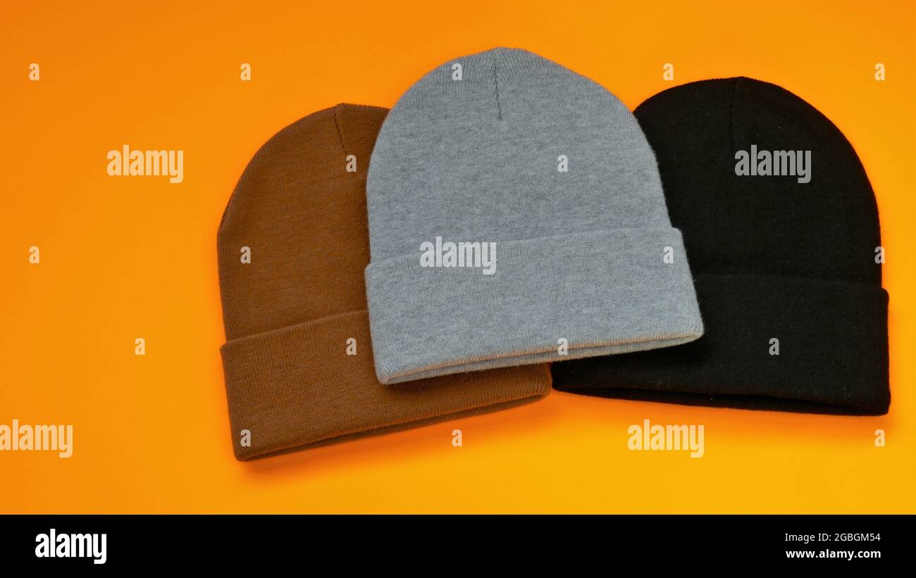 Beanie-Hüte auf einem leuchtend orangefarbenen Hintergrund gesetzt. Graue, schwarze und braune Strickmützen. Stockfoto