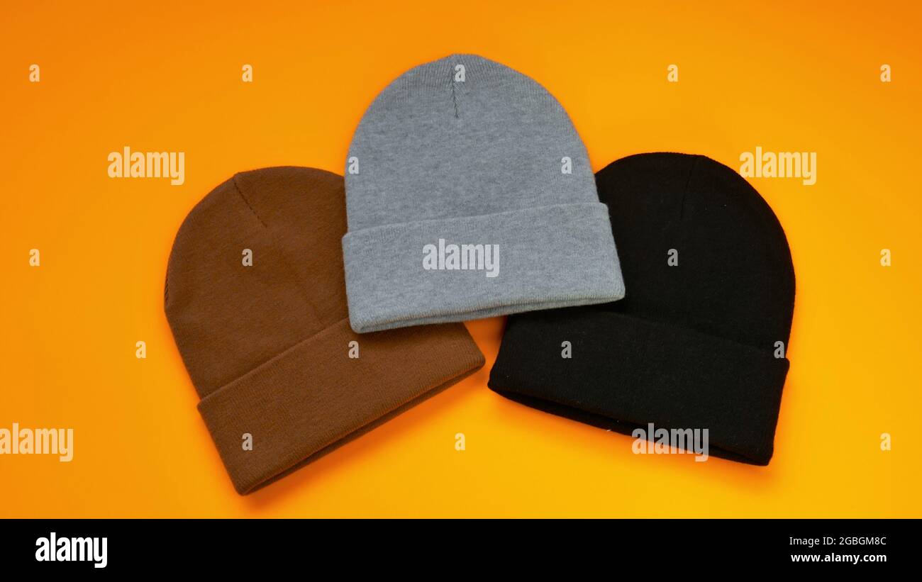 Beanie-Hüte auf einem leuchtend orangefarbenen Hintergrund gesetzt. Graue, schwarze und braune Strickmützen. Modische Hüte Stockfoto