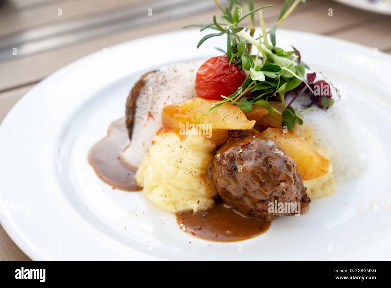 Fleischbällchen aus Hackfleisch mit Gurkengemüse, Kartoffelpüree und Sauce, garniert mit Tomaten, Kräutern und Sprossen auf einem weißen Teller, Modern gourm Stockfoto