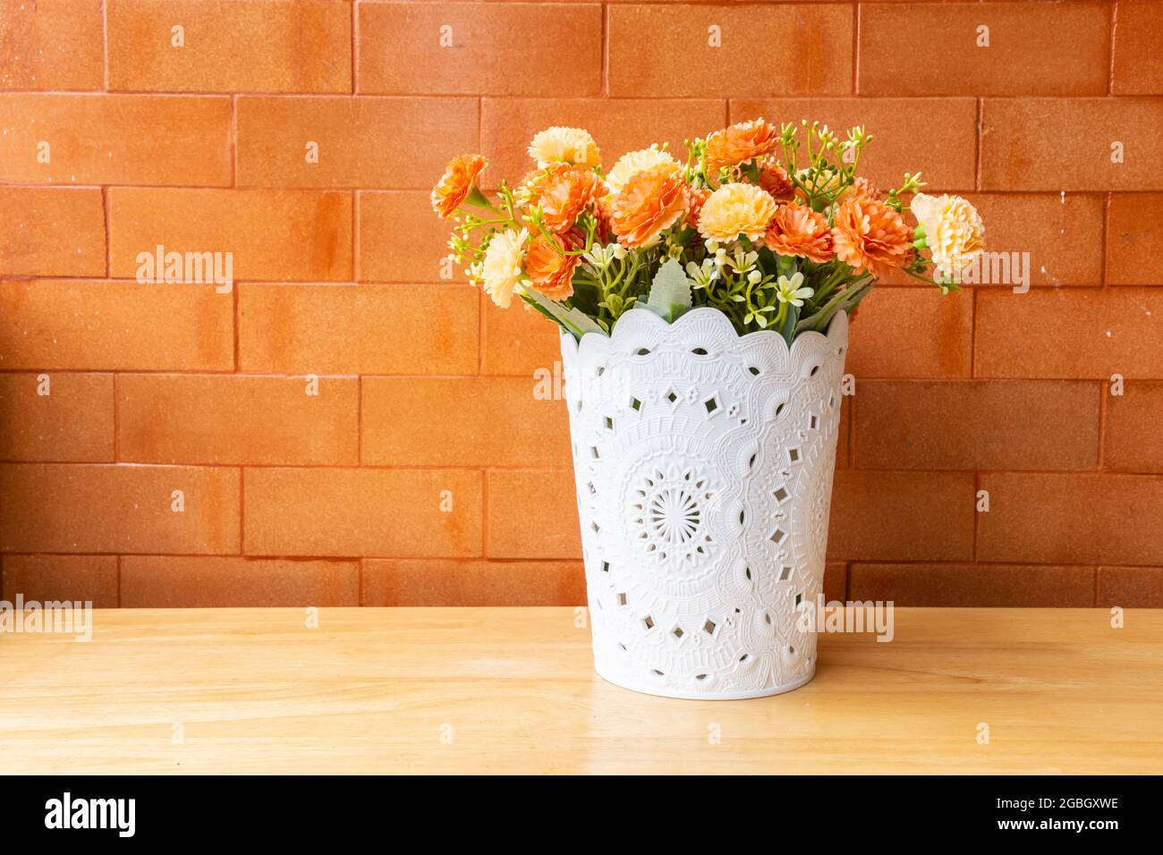 Mockup Blume auf einem Holztisch mit einem Backstein Wand orange Hintergrund. Stockfoto