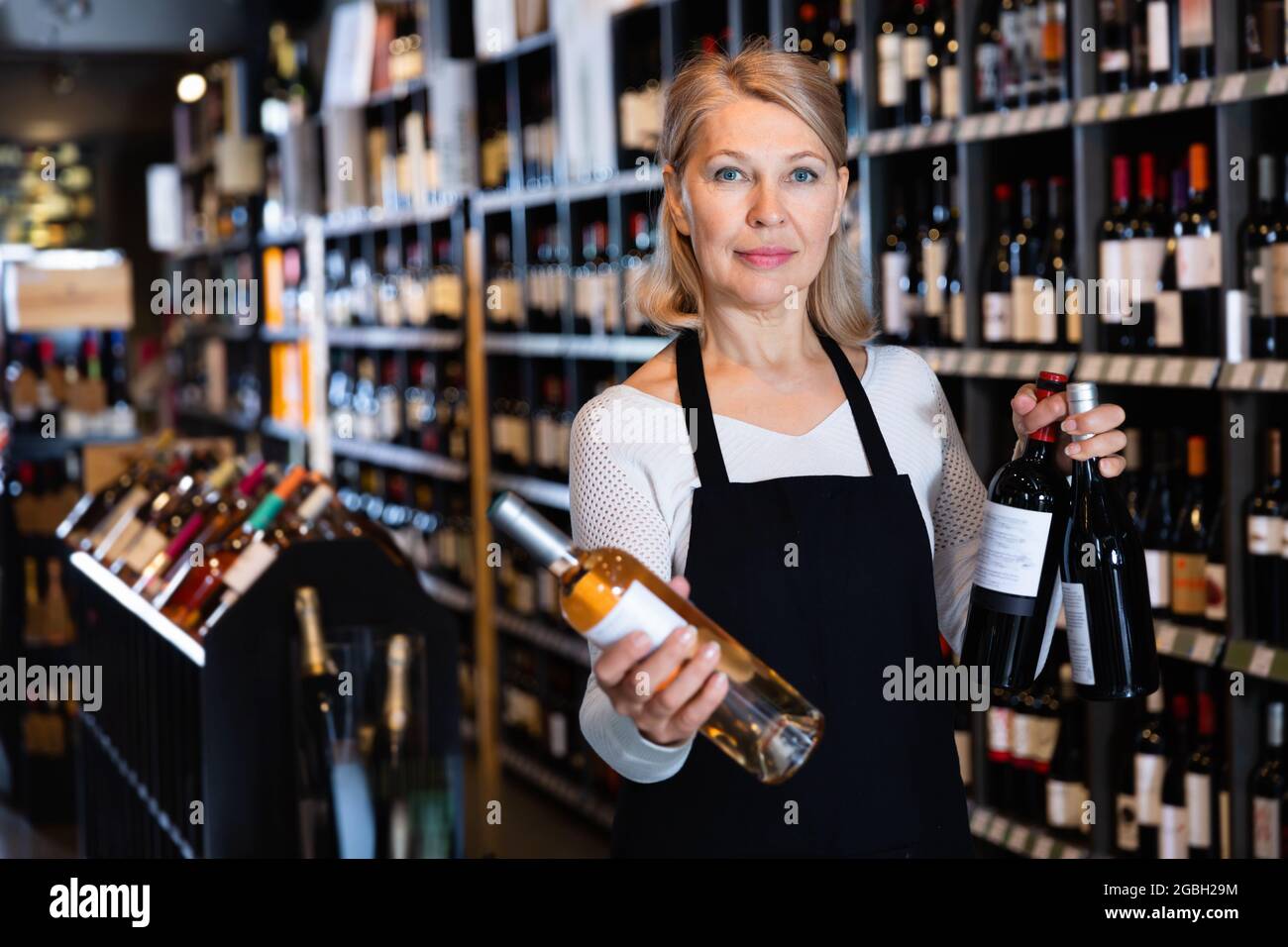 Lächelnd qualifizierte reife Verkäuferin bietet natürliche Weine in Flaschen zum Verkauf an Weingut Stockfoto