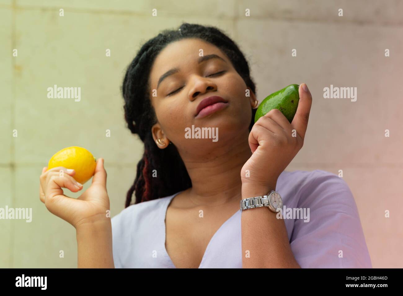 Wunderbare junge Afro-Frau mit Avocado und Zitrone in den Händen. Popularisierung der Rohkost. Werbung Stockfoto