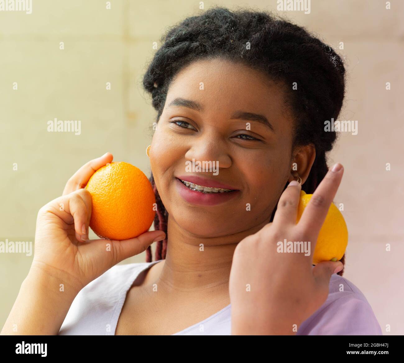 Fröhliche junge Afro-Frau mit Orange und Zitrone in den Händen. Förderung eines gesunden Lebensstils Stockfoto