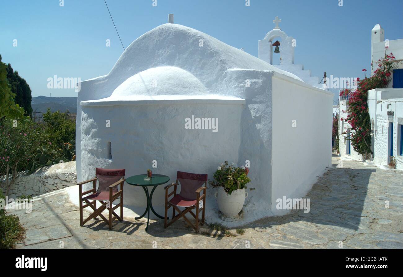 Schöne griechische Kirche, Insel Amorgos, Kykladen, Griechenland. Tische und Stühle am charmanten alten und traditionellen Gebäude am Dorfplatz. Stockfoto