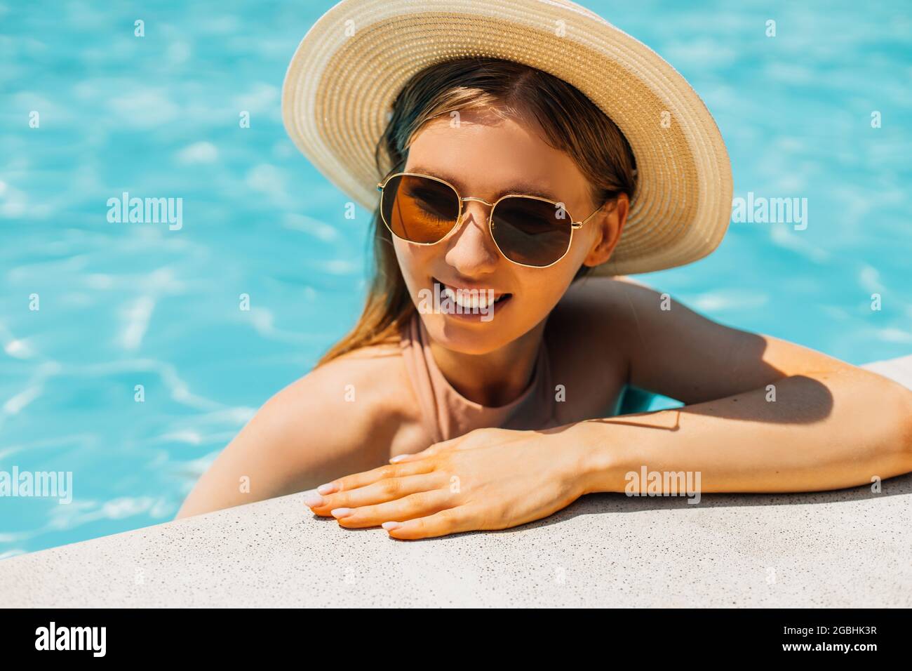 Schöne junge gebräunte Frau in Sonnenbrille und Sommerhut, im Außenpool, Frau in einem Badeanzug Sonnenbaden im Pool, glückliche Frau in Th entspannen Stockfoto