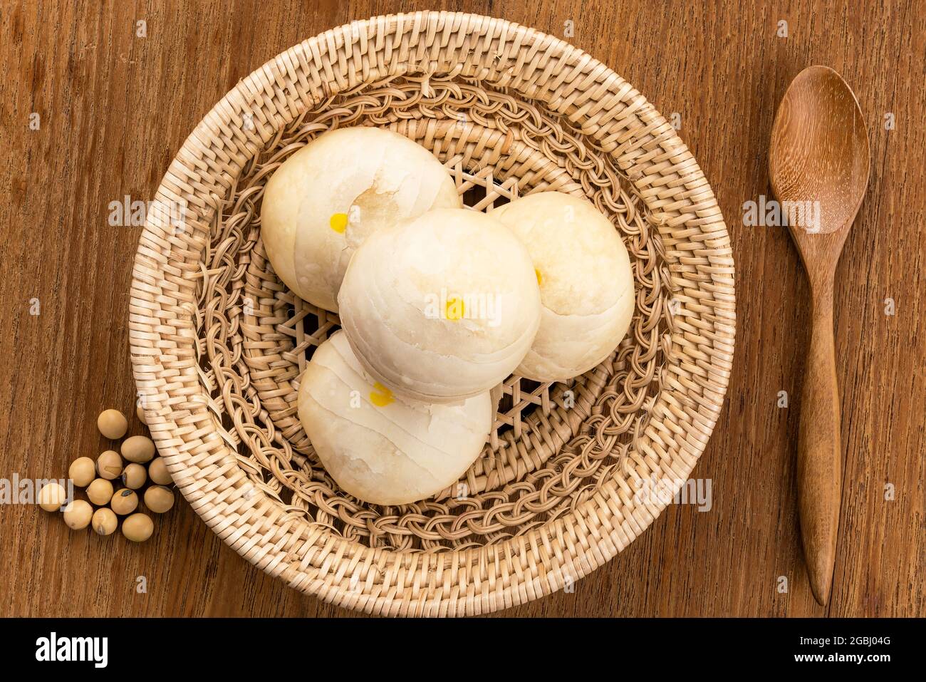 Draufsicht auf chinesisches Gebäck oder Mondkuchen gefüllt mit süßer Mungbohnenpaste und gesalzenem Eigelb in Bambuskorb mit Holzlöffel und Sojabohne auf Holz Stockfoto
