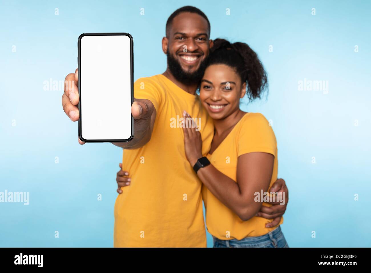 Neue tolle mobile App. Afroamerikanisches Paar präsentiert Smartphone mit Mockup, Förderung der Anwendung oder Website Stockfoto