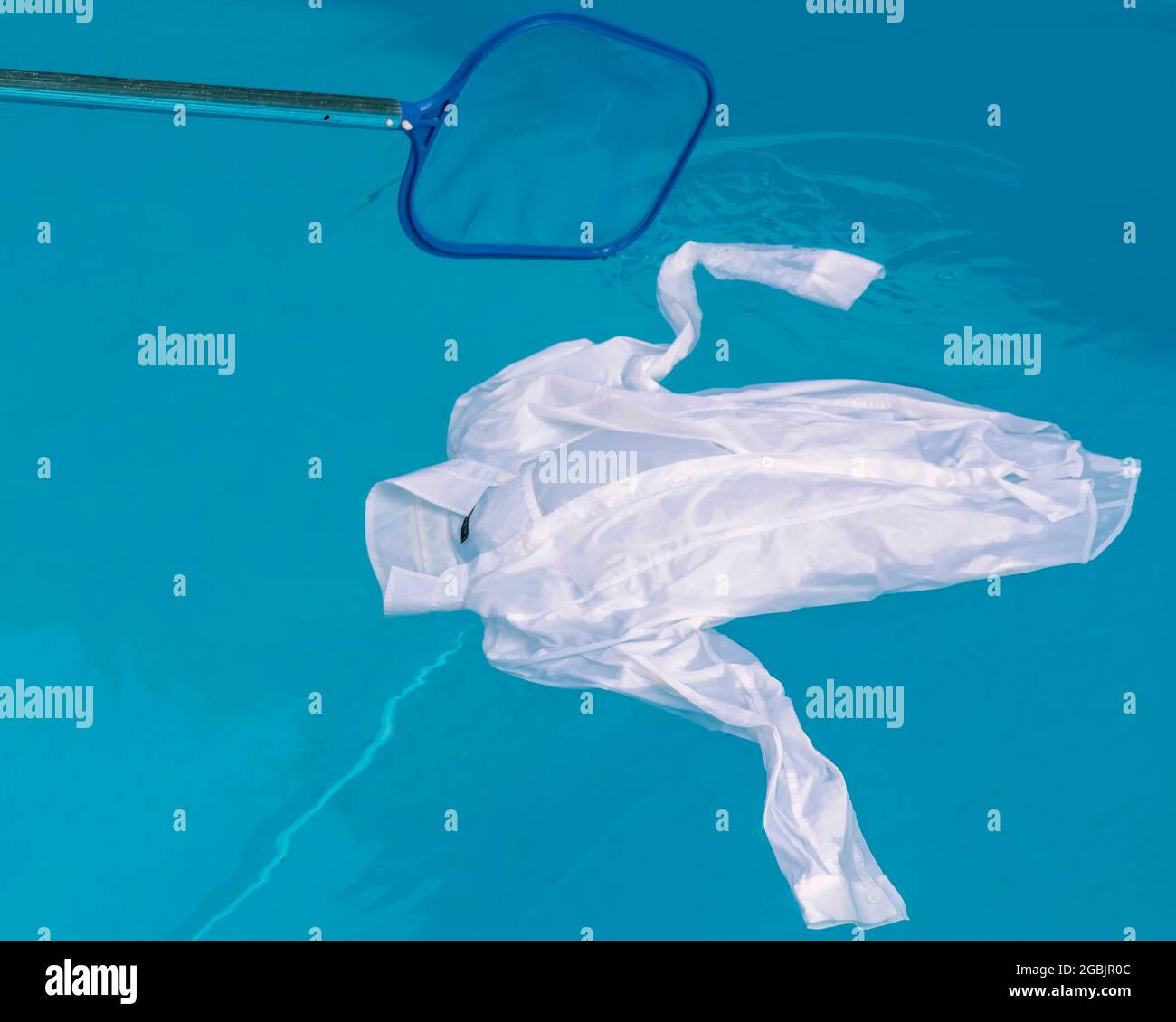Ein weißes Hemd schwebt auf dem Wasser eines Schwimmbeckens, während jemand versucht, es mit einem Netz zu fischen Stockfoto