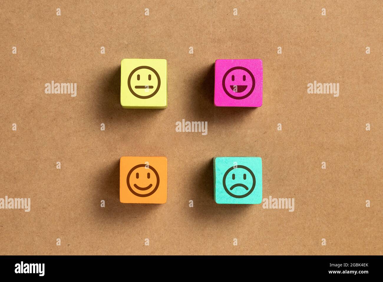 Emoticon Gesichter in Farben Holzblöcke über braunem Holzpapier. Konzepte zur Servicebewertung und Zufriedenheitsumfrage. Wütend, neutral, gute Laune und glücklich Stockfoto