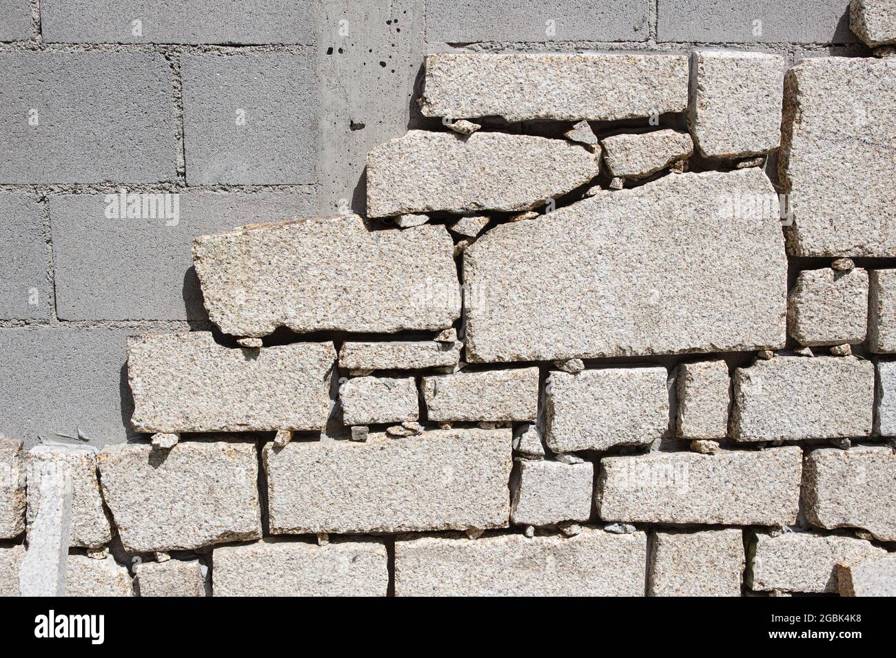 Detail der Cinder Blockwand, die auf der Außenbaustelle mit Granitsteinplatten ausgekleidet ist. Wanddekoration Stockfoto