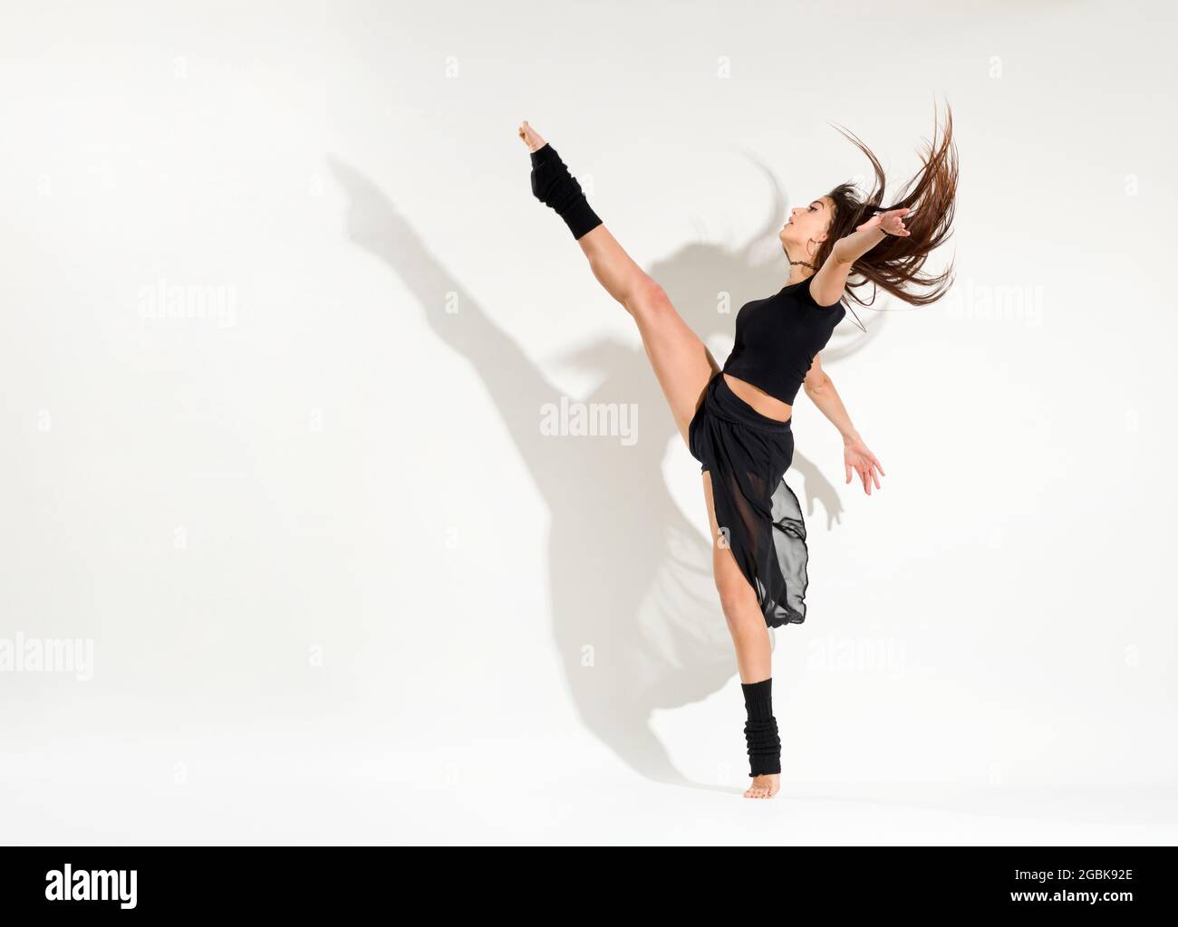 Agil fit junge Frau macht eine Eiskunstläuferin dynamische Entwicklung Pose ihre Haare und heben ihr Bein auf hoch über weiß mit einem Schatten und Copyspace Stockfoto