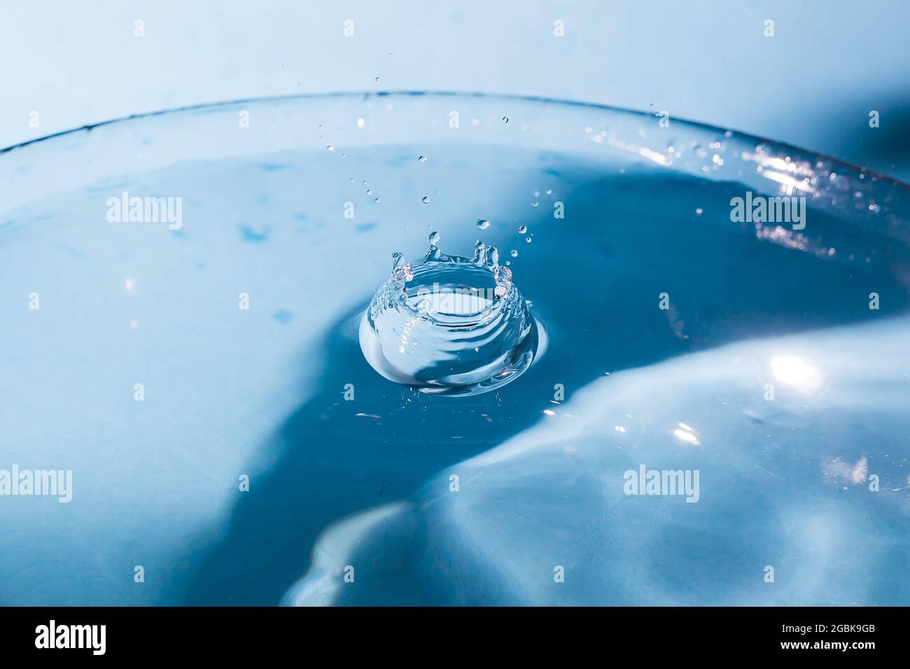 Wasser spritzt kronenförmig und fällt herab. Spritzer der fallenden Wassertropfen. Wassertropfen auf blauem Hintergrund. Blaue Wasseroberfläche mit Spritzer. Cle Stockfoto