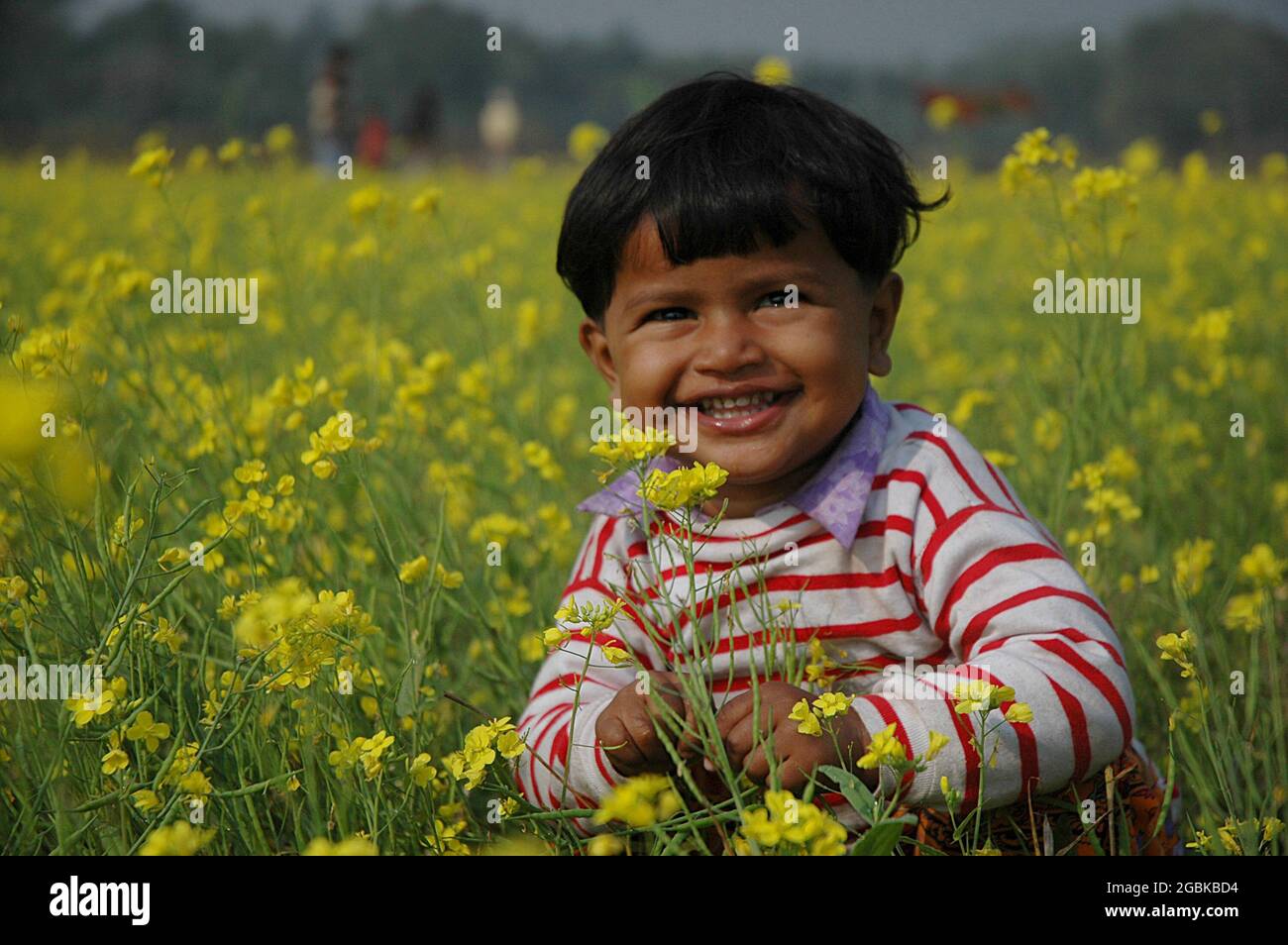 Ein lächelndes Kind inmitten eines Senffeldes. Hasempur, Jessore, Bangladesch. 4. Januar 2008. Stockfoto