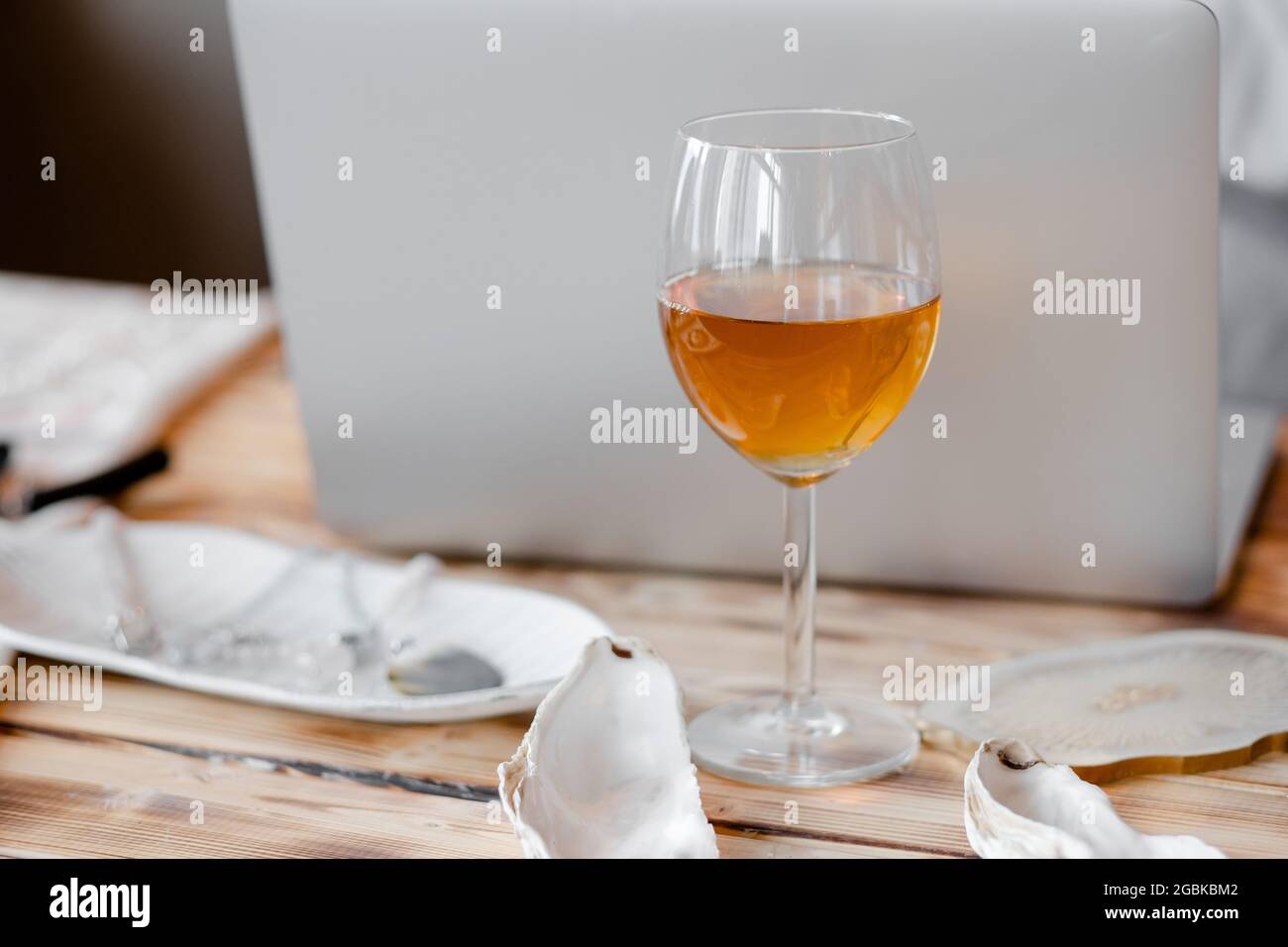 Ein Glas Weißwein auf dem Hintergrund eines Laptops. Weinglas auf einem hölzernen Hintergrund. Entspannen Sie sich bei der Arbeit Stockfoto