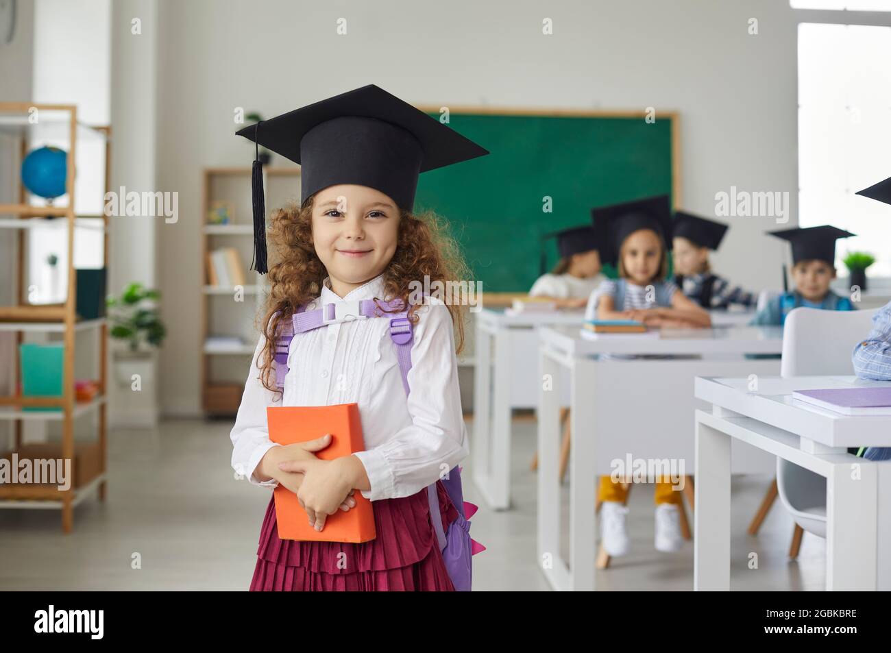 Porträt eines schönen kleinen lockigen Grundschulabsolventen Mädchen trägt einen akademischen Hut. Stockfoto