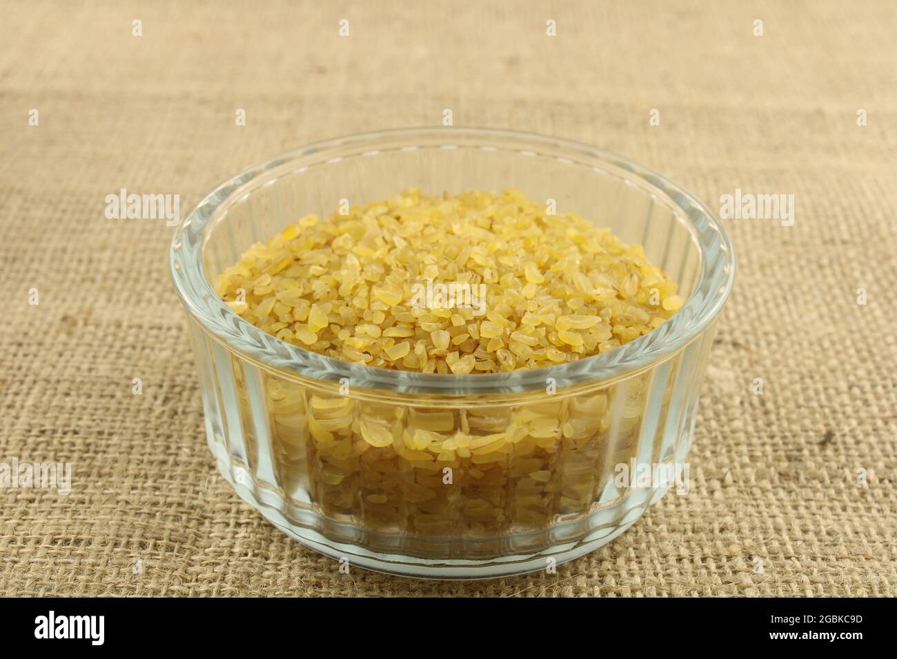 Roher grober Bulgur-Weizen in einer Glasschale auf braunem hessischen Hintergrund Stockfoto